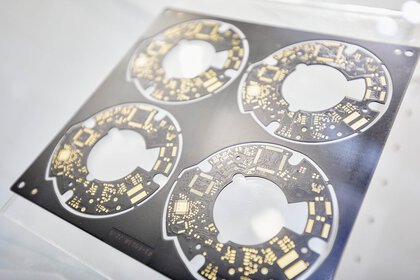 Close-up of four identical round circuit boards still hanging in a black die-cut mould.