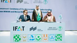Drei Männer bei einer Vertragsunterzeichnung mit Bannern der IFAT und der Messe München, Logos und einem Dekorationstisch.