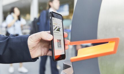 Person, die an einer Ticketschranke einen QR-Code auf ihrem Smartphone scannt.