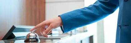 A person in a blue jacket rings a service bell on a counter.