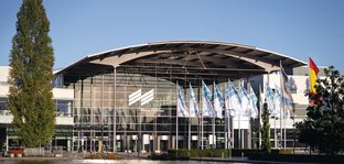 Exterior shot of the west entrance to Messe München with the trade fair lake and flags in the foreground