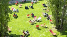 Visitors to transport logistic relax in numerous red deckchairs on a sunlit green area between the exhibition halls.